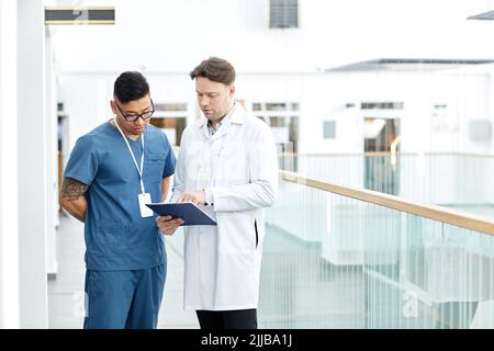 Portrait de deux médecins regardant le presse-papiers tout en se tenant sur le balcon dans l'intérieur moderne de la clinique, l'espace de copie Banque D'Images