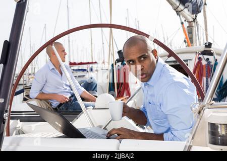 homme travaillant à l'ordinateur portable et de boire du café et regardant les passants sur des yachts privés dans le port maritime Banque D'Images