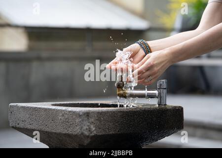 Mains avec l'eau qui coule du robinet dans la rue. Des gouttes d'eau s'incoutent sur les doigts de la jeune fille. Banque D'Images