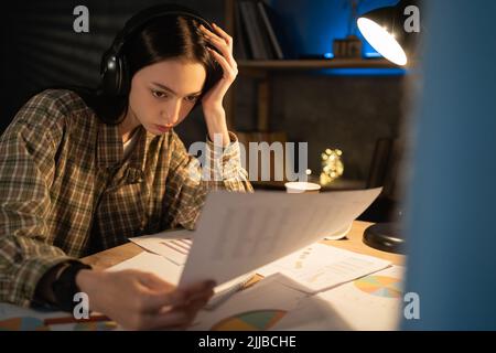 Une jeune femme d'affaires asiatique concentrée travaillant avec des papiers sur un projet la nuit à la maison, une étudiante japonaise concentrée envisage la paperasserie Banque D'Images