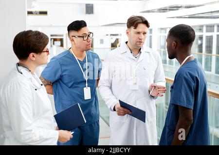 Divers groupes de médecins se tenant en cercle et discutant du travail en clinique moderne Banque D'Images