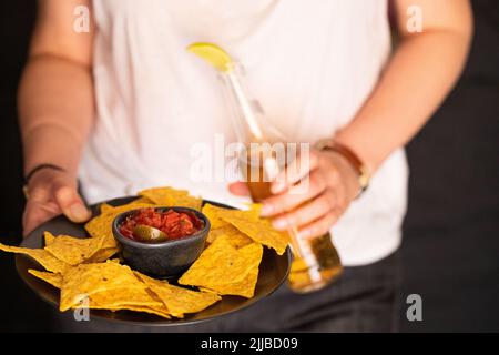 Assiette pour les mains des femmes avec plat mexicain, sauce au piment rouge nachos et bouteille de bière. Style de vie cuisine de rue. Banque D'Images