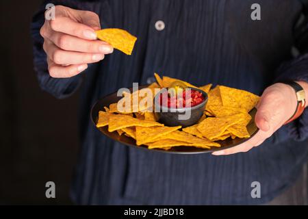 Les mains des femmes tenant le bois essayer avec des nachos mexicains avec sauce Chili rouge. Style de vie cuisine de rue. Banque D'Images