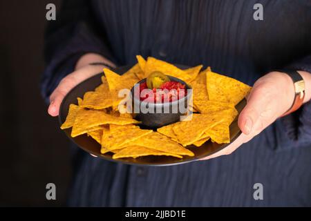 Les mains des femmes tenant le bois essayer avec des nachos mexicains avec sauce Chili rouge. Style de vie cuisine de rue. Banque D'Images