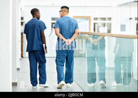 Vue arrière de deux médecins portant un uniforme bleu marchant dans le hall de la clinique moderne, espace copie Banque D'Images