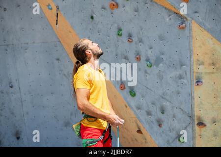 Un homme se concentre avant d'escalader, debout sur le fond d'un mur d'escalade. Banque D'Images