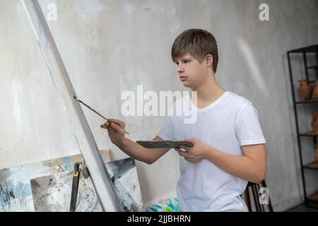 Un garçon avec le syndrome de Down peinture dans le studio et regardant impliqué Banque D'Images