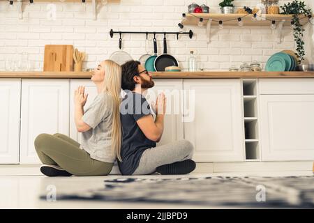 Jeune couple de caucasiens dans la cuisine faisant la pose de prière de yoga. Femme blonde et homme aux cheveux foncés avec des lunettes et une barbe. Prise de vue en intérieur. Photo de haute qualité Banque D'Images