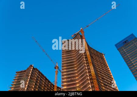 Bâtiments de plusieurs étages en construction avec grues de construction contre le ciel bleu au coucher du soleil Banque D'Images