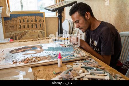 Un artiste, avec une image du célèbre amphithéâtre romain derrière lui, travaille sur un nouveau mosiac fait de petits fragments de pierre colorée à El Jem, en Tunisie. E Banque D'Images