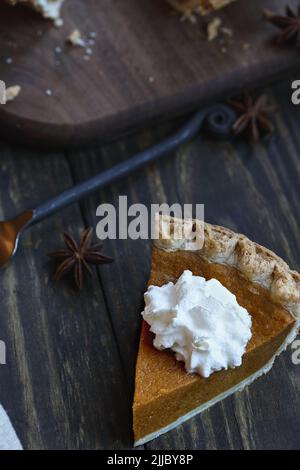 Une tranche de tarte à la citrouille fraîche sur fond de bois. Mise au point extrême sélective sur la crème fouettée avec un premier plan et un arrière-plan flous. Banque D'Images