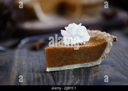 Une tranche de tarte fraîche à la citrouille avec de la crème fouettée sur une table en bois. Mise au point extrême sélective sur la crème fouettée avec le premier plan flou et Banque D'Images