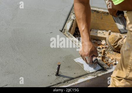 Un ouvrier de maçonnerie tient une truelle d'acier et lisse un plancher de ciment avec du béton de plâtrage Banque D'Images