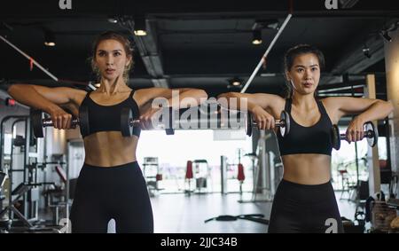 Deux filles sportives font des exercices avec des haltères dans la salle de gym. Banque D'Images