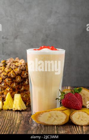 Smoothie à la banane, aux fraises et à l'ananas sur une table en bois et thé moussant ou boules de thé boba Banque D'Images