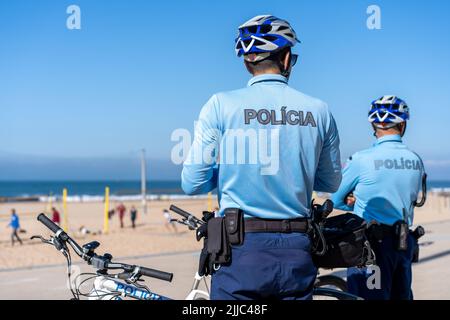 Deux policiers patrouillent sur la promenade du bord de mer à vélo. Les gens brûlent le soleil sur la plage publique de la ville, sur la côte Atlantique. Patrouille de police à vélo le Banque D'Images