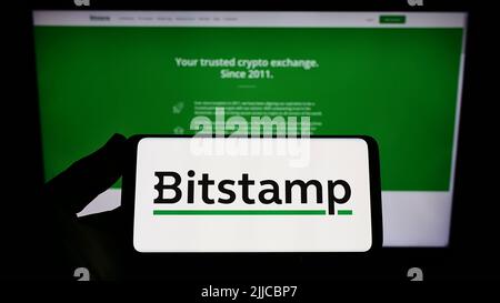 Personne détenant un smartphone avec le logo de la société d'échange de crypto-monnaies Bitstamp Ltd. À l'écran devant le site Web. Mise au point sur l'affichage du téléphone. Banque D'Images