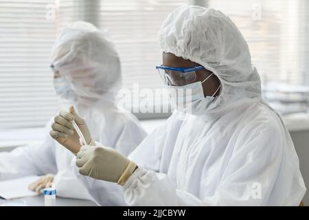 Portrait de jeunes scientifiques féminins portant un équipement de protection complet tout en effectuant des recherches avec des échantillons dangereux dans un laboratoire médical, espace de copie Banque D'Images