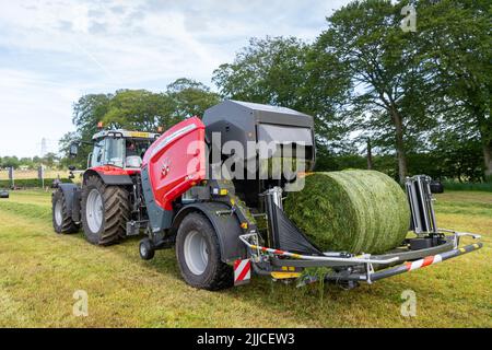 Mise en balle d'herbe sur un pré à l'aide d'un tracteur Massey Ferguson, d'une presse à balles et d'une enrubanneuse 3130DF. Dumfries, Écosse. Banque D'Images