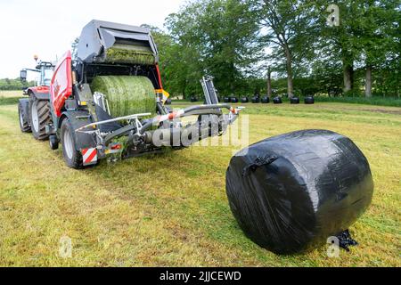 Mise en balle d'herbe sur un pré à l'aide d'un tracteur Massey Ferguson, d'une presse à balles et d'une enrubanneuse 3130DF. Dumfries, Écosse. Banque D'Images