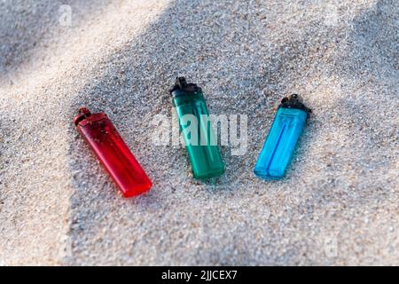 Trois briquets, rouge, vert et bleu, posés sur le sable, polluant la plage et les mers Banque D'Images