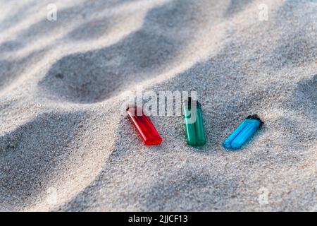 Trois briquets, rouge, vert et bleu, posés sur le sable, polluant la plage et les mers Banque D'Images