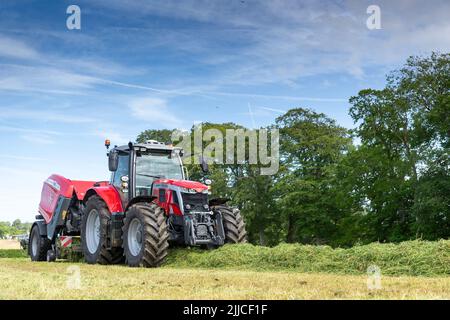 Mise en balle d'herbe sur un pré à l'aide d'un tracteur Massey Ferguson, d'une presse à balles et d'une enrubanneuse 3130DF. Dumfries, Écosse. Banque D'Images