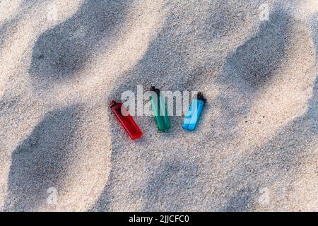 Trois briquets, rouge, vert et bleu, posés sur le sable, polluant la plage et les mers Banque D'Images