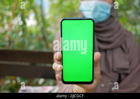 jeunes femmes avec masque de visage montrant à l'aide d'un smartphone avec écran vert Banque D'Images