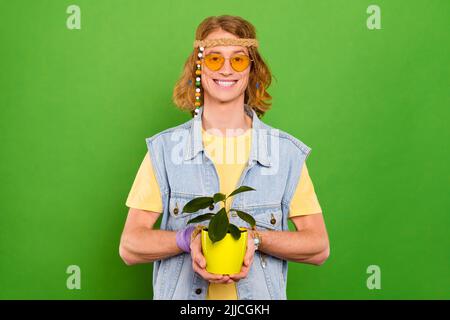 Portrait d'un sympathique gars gai tenant l'usine dans les mains en croissance isolée sur fond vert clair de couleur Banque D'Images