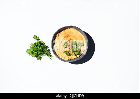 Pose à plat. Persil et bol avec houmous de pois chiches, parsemés de paprika, isolés sur fond blanc. Copier l'espace Banque D'Images