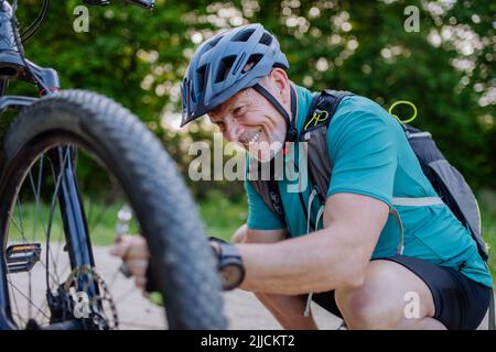 Homme senior actif répare un vélo, pompe des pneus dans la nature en été. Banque D'Images