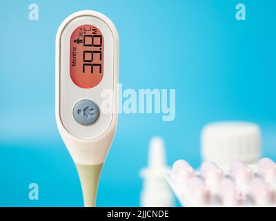 Le thermomètre pour mesurer la température du corps indique une température élevée. Thermomètre numérique médical et médicaments sur fond bleu. Banque D'Images