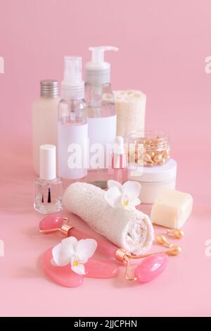 Pots cosmétiques naturels, accessoires pour le soin de la peau et masseurs à quartz rose avec fleur d'orchidée blanche sur gros plan rose clair. Maquette de produits de beauté. VÉ Banque D'Images