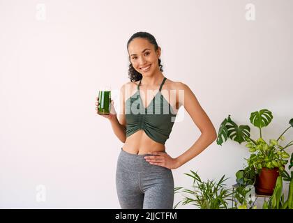 Une belle femme multi-ethnique sourit avec du jus vert - épinards, kale, vitamans Banque D'Images