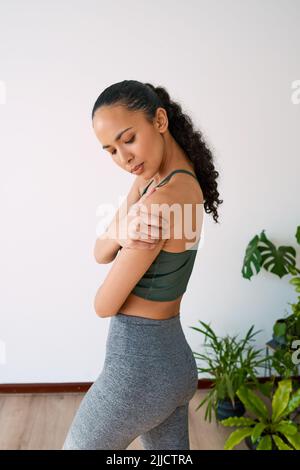 Une jeune femme multi-ethnique tient son épaule dans la douleur pendant le yoga Banque D'Images