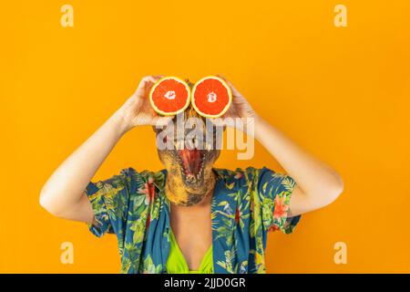 Femme méconnaissable dans un masque de dinosaure tenant ses yeux des tranches d'orange de sang frais. Une alimentation surréaliste et saine. Banque D'Images