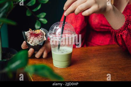 Latte au matcha glacé et gros gâteau dans un café entre les mains des femmes. Banque D'Images