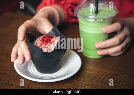 Latte au matcha glacé et gros gâteau dans un café entre les mains des femmes. Banque D'Images