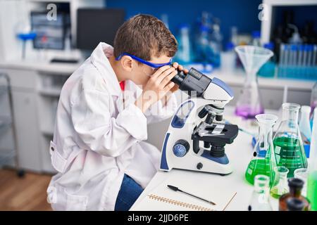 Enfant blond portant l'uniforme scientifique au microscope en laboratoire Banque D'Images