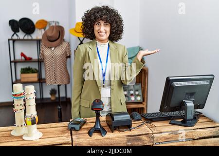 Jeune femme du Moyen-Orient travaillant en tant que gestionnaire à la boutique de vente au détail souriant gai présenter et pointer avec la paume de la main regardant l'appareil photo. Banque D'Images
