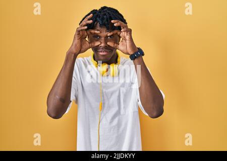 Jeune homme africain avec des dreadlocks debout sur fond jaune essayant d'ouvrir les yeux avec les doigts, endormi et fatigué pour la fatigue matinale Banque D'Images