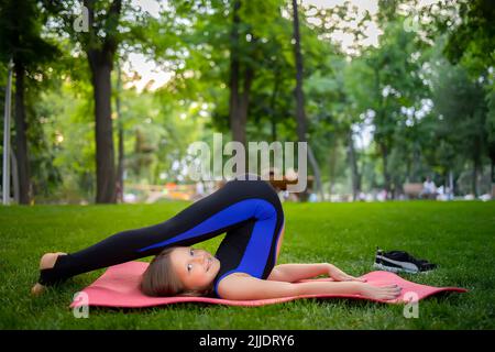 une petite fille exécute des éléments de yoga en levant les jambes et en se pliant Banque D'Images