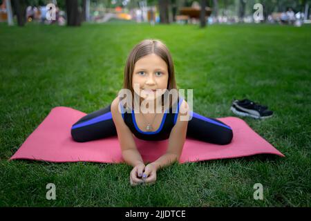 dans le parc, une petite fille exécute un élément de grenouille, en étirant sur un tapis Banque D'Images