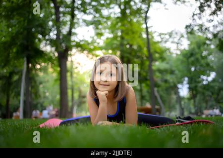 dans le parc, une petite fille exécute un élément de grenouille, en étirant sur un tapis Banque D'Images