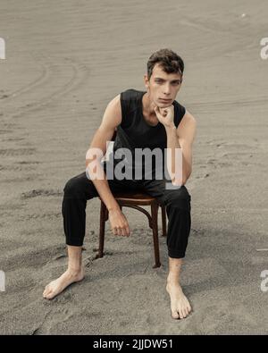 Jeune homme solitaire assis sur une chaise dans le désert Banque D'Images