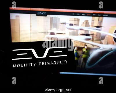 Personne tenant un téléphone portable avec le logo de la société Eve Holding Inc. (Eve Air Mobility) à l'écran en face de la page Web d'affaires. Mise au point sur l'affichage du téléphone. Banque D'Images