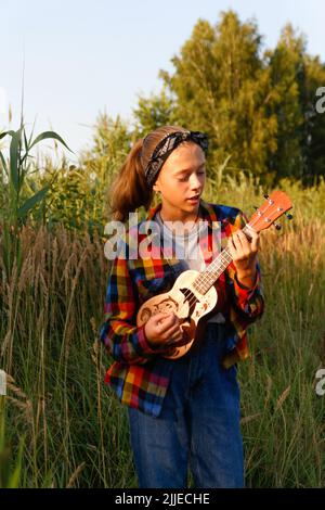 Reflous la jeune fille avec de la guitare. Jeune fille marchant sur fond de nature. Petite fille dehors sur la prairie verte. Génération z. Automne. Bandana. Style de vie. D Banque D'Images