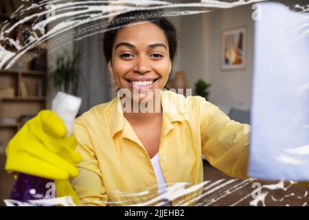Femme noire nettoyant vitres avec Rag et détergent intérieur Banque D'Images