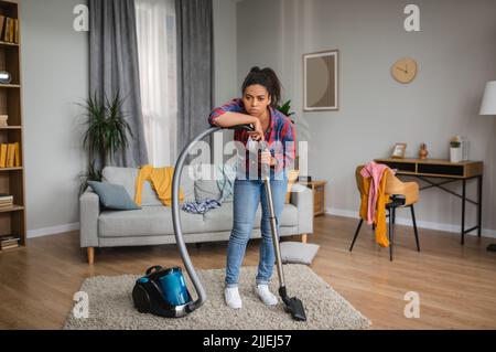 Malheureux fatigué triste millénaire afro-américaines femme au foyer passer l'aspirateur et se reposer du nettoyage Banque D'Images